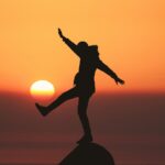 Persoon balanceert op &eacute;&eacute;n been bij zonsondergang als metafoor voor stabiliteit, grip en wendbaarheid